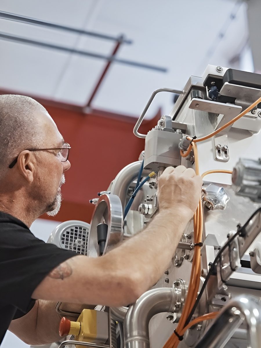 A person in a black shirt is working with a complex machine in an industrial setting. The scene conveys focus and technical expertise.