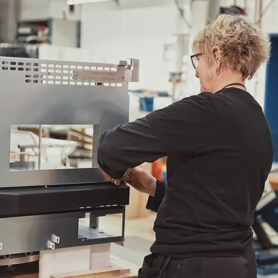 A person with short blonde hair works on assembling a large metallic machine part in a workshop, conveying focus and technical skill.