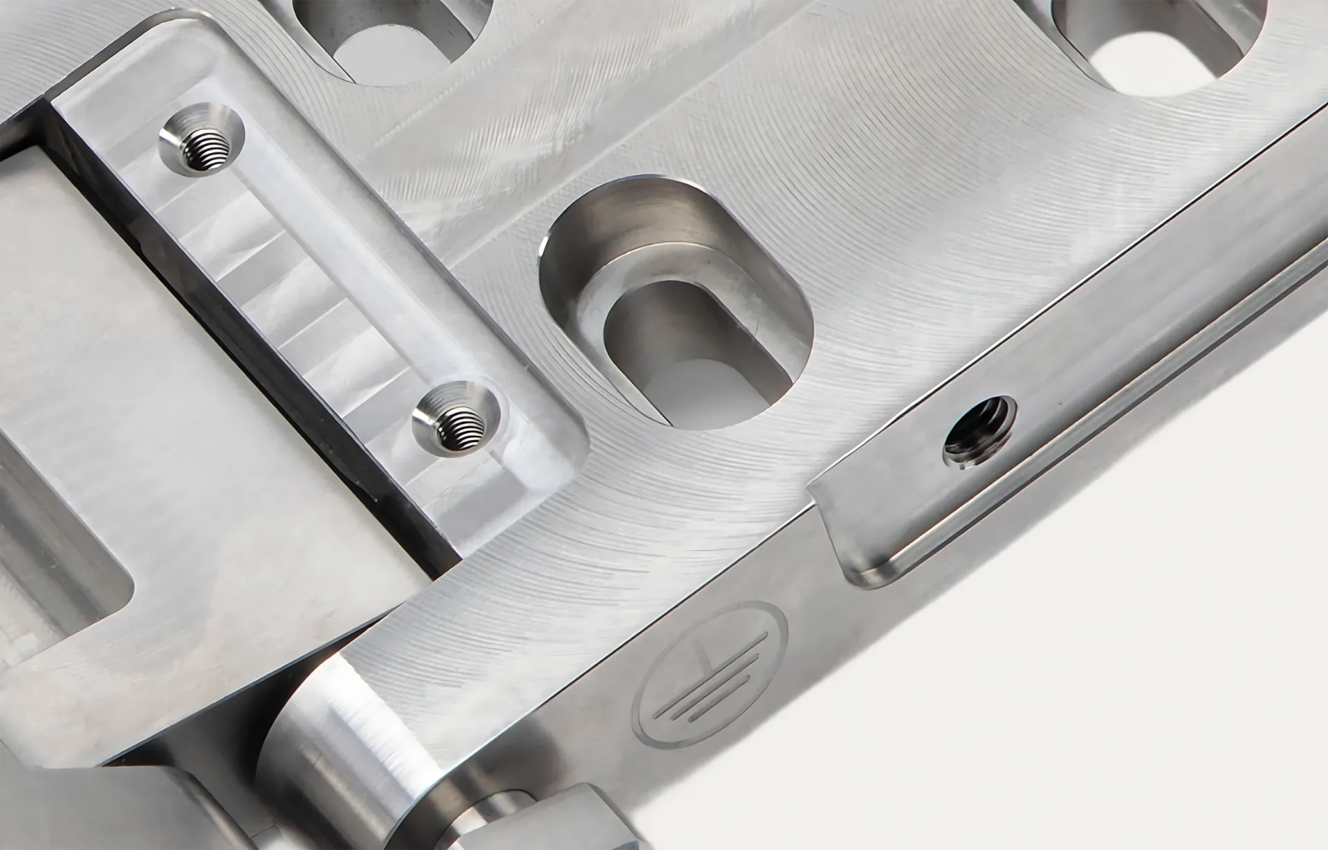 Close-up of a polished metal surface featuring grooves, circular indentations, and a threaded hole, conveying precision and industrial craftsmanship.
