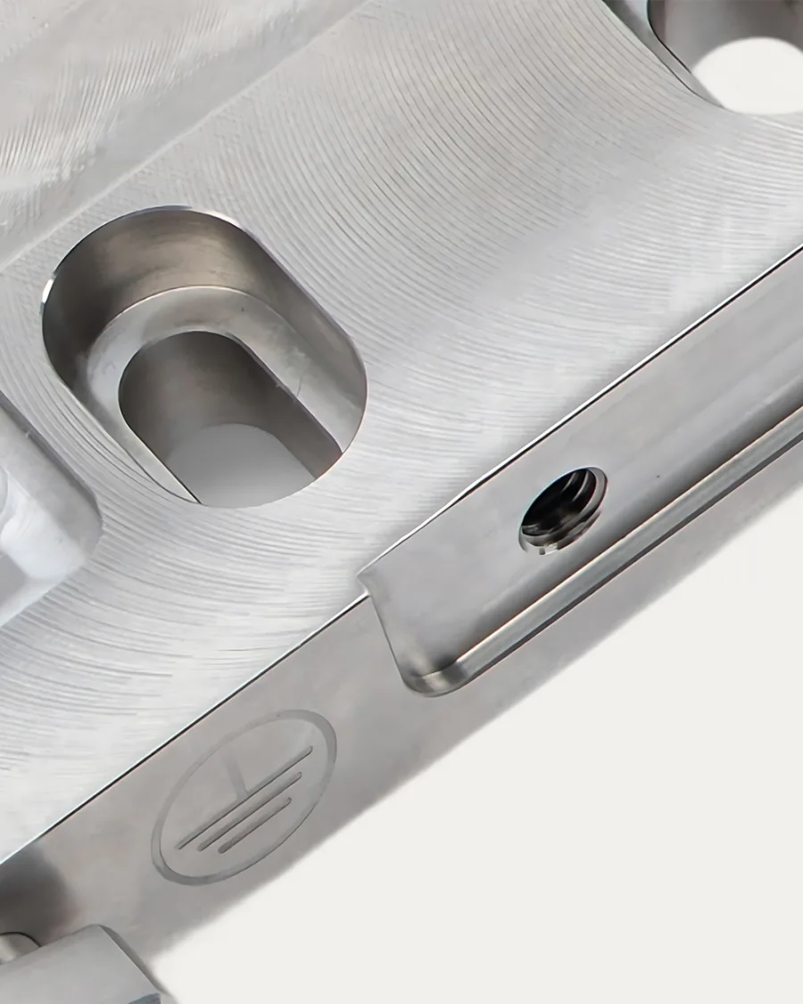 Close-up of a polished metal surface featuring grooves, circular indentations, and a threaded hole, conveying precision and industrial craftsmanship.