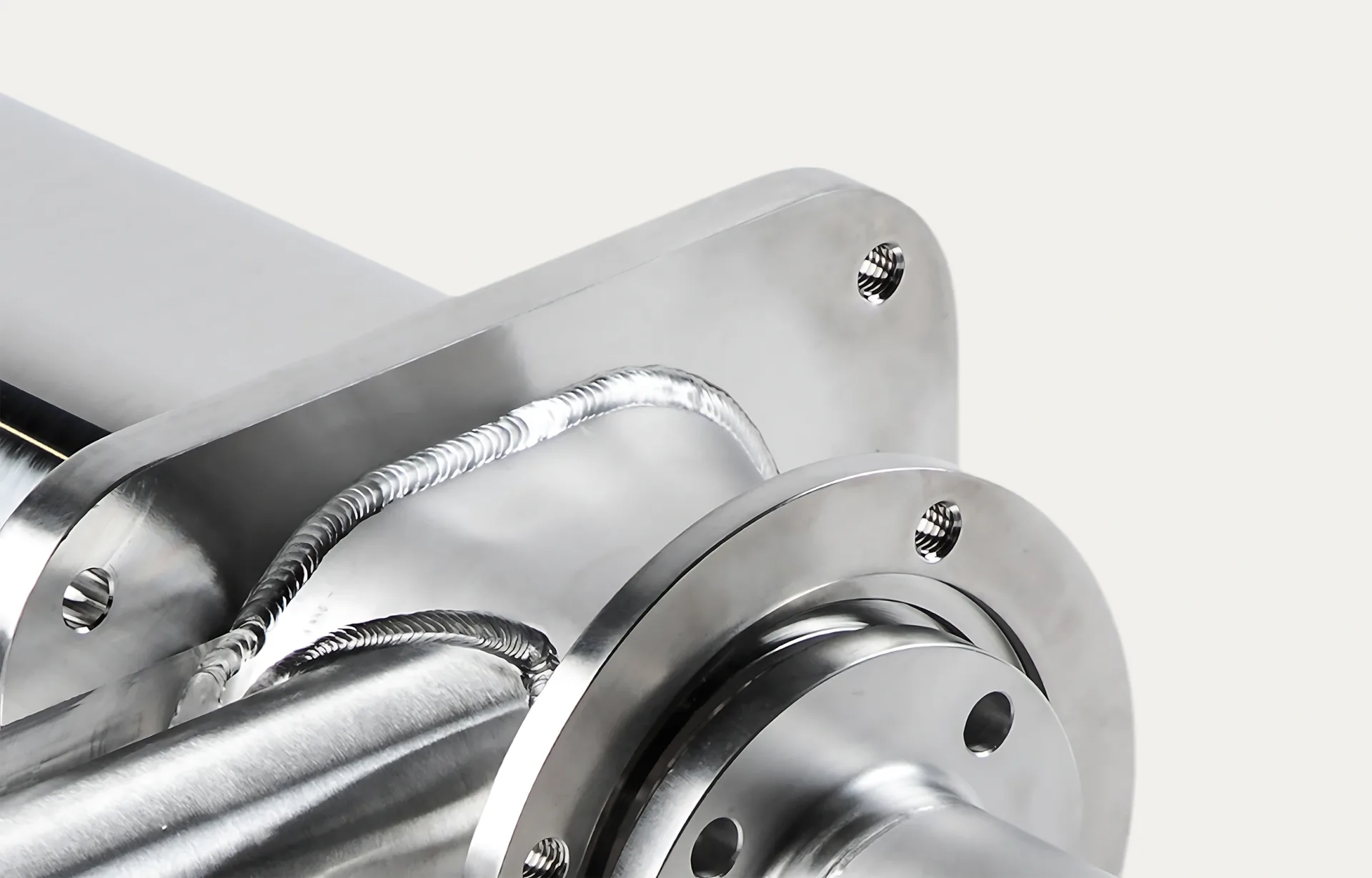 Close-up of a polished metal machine part with precise welding lines and drilled holes, conveying precision engineering and industrial craftsmanship.