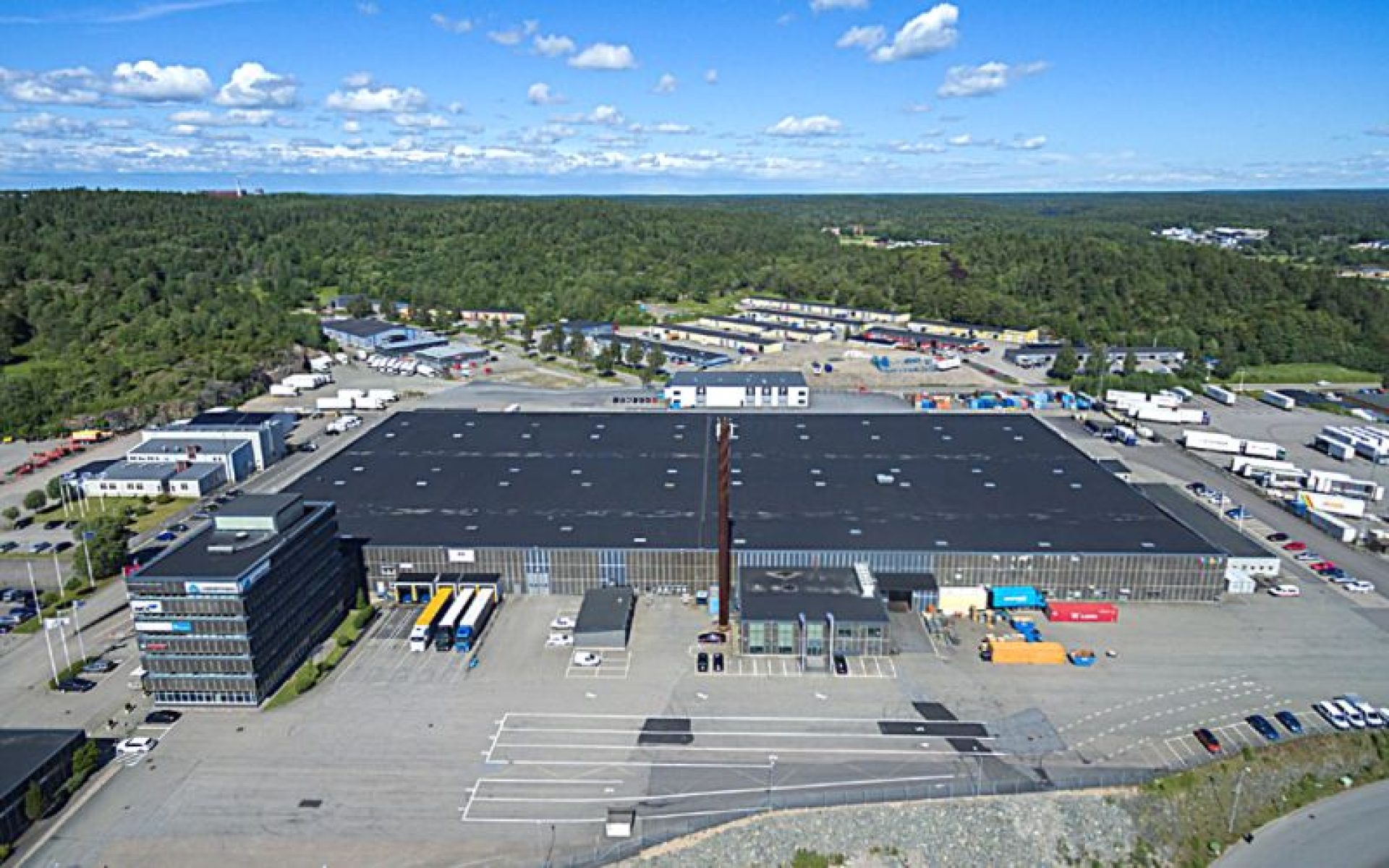 Aerial shot of a black and gray factory surrounded by trucks, cars and forrest.