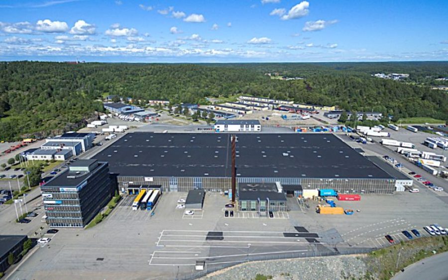 Aerial shot of a black and gray factory surrounded by trucks, cars and forrest.