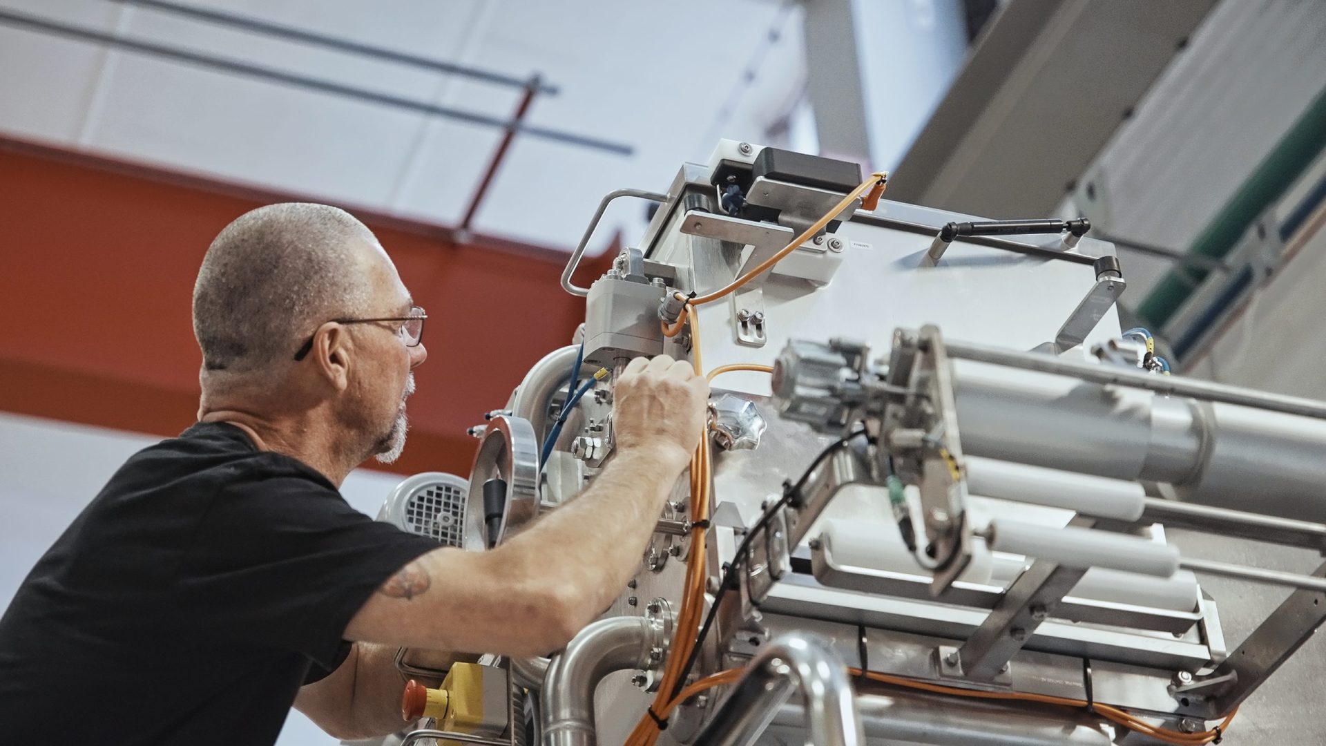 A person in a black shirt is working with a complex machine in an industrial setting. The scene conveys focus and technical expertise.